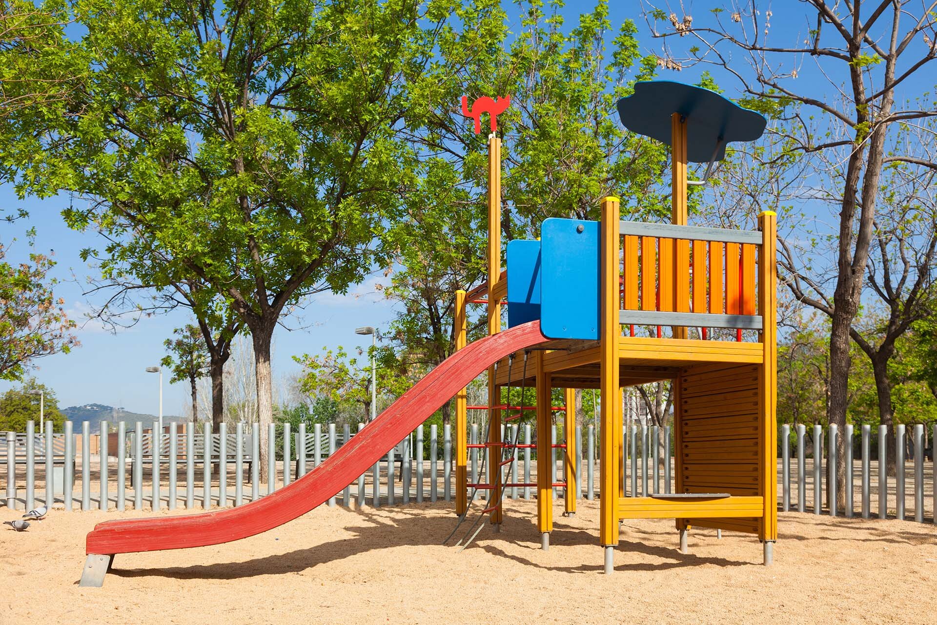 Sicherer Spielbereich mit farbenfrohem Klettergerüst und Rutschbahn | © stock.adobe.com Spielplatz mit Rutsche und Fallschutzbelag unter sonnigem Himmel | © stock.adobe.com