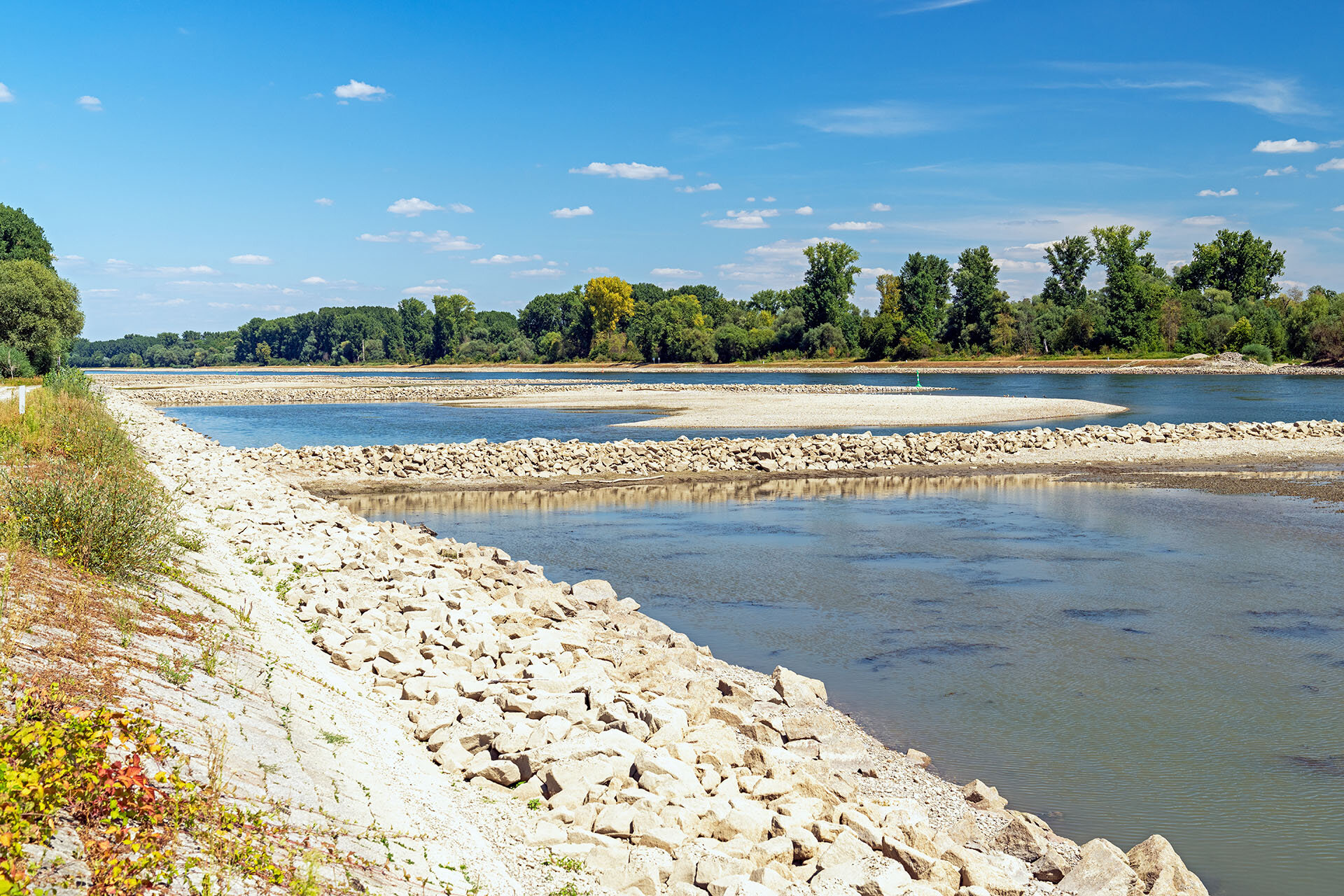 Natürliches Kiesufer mit Blick auf den Fluss | © stock.adobe.com Kiesufer an einem Fluss mit Vegetation im Hintergrund | © stock.adobe.com