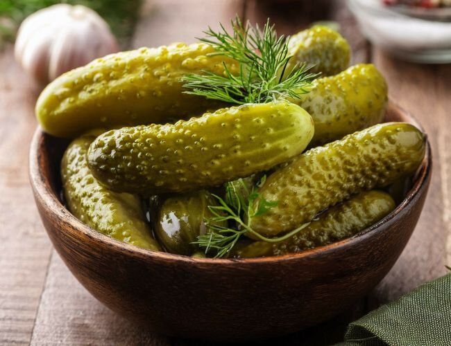 Essiggurken in Holzschale mit Kräutern angerichtet | © stock.adobe.com